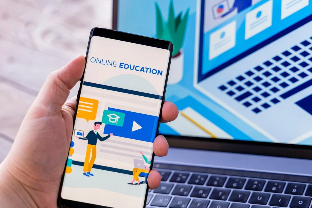 Man using education app on smartphone with laptop in background.